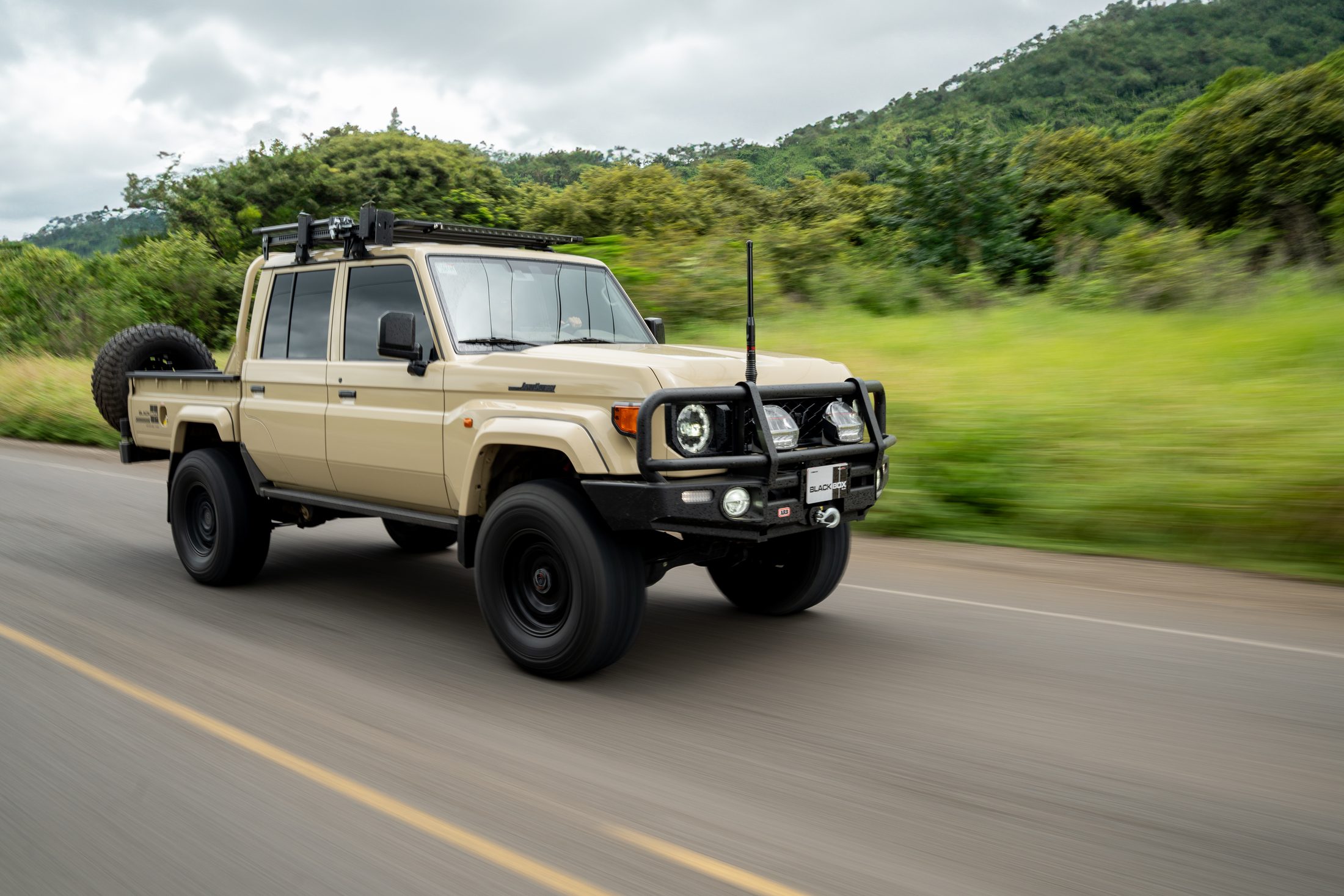 Beige Toyota Land Cruiser 70 double cab driving on a country road, panning shot, photographed by Maxime Hugo